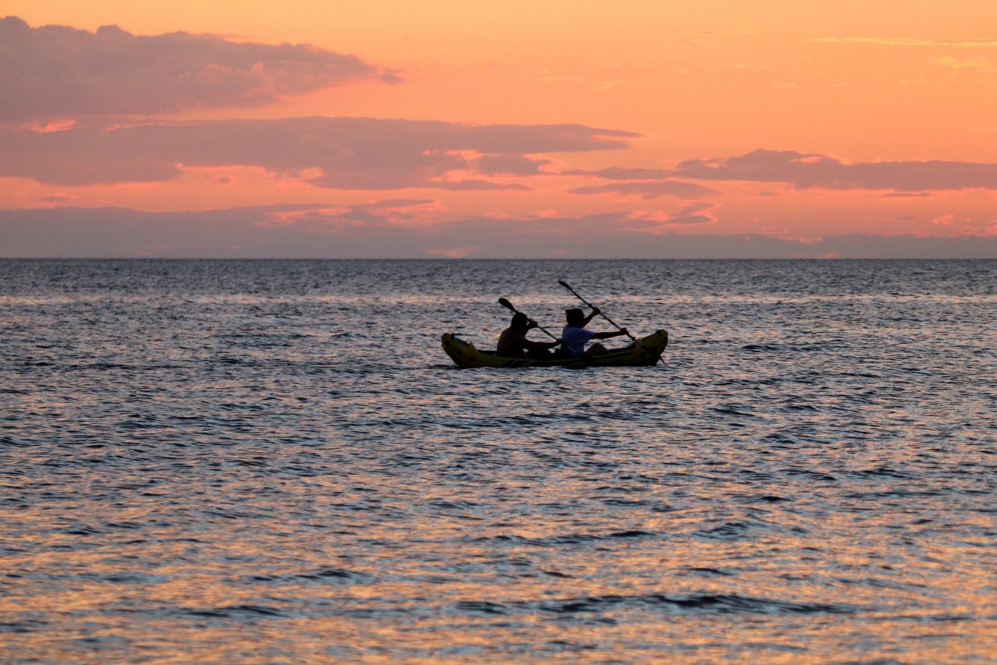 A couple of people sitting in a small boat, surrounded by the vast blue ocean under a clear sky.