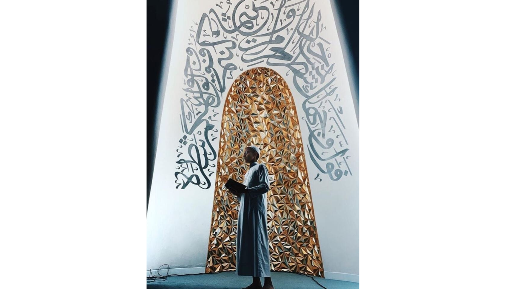 A man stands in front of a large Arabic wall, showcasing intricate designs and calligraphy.