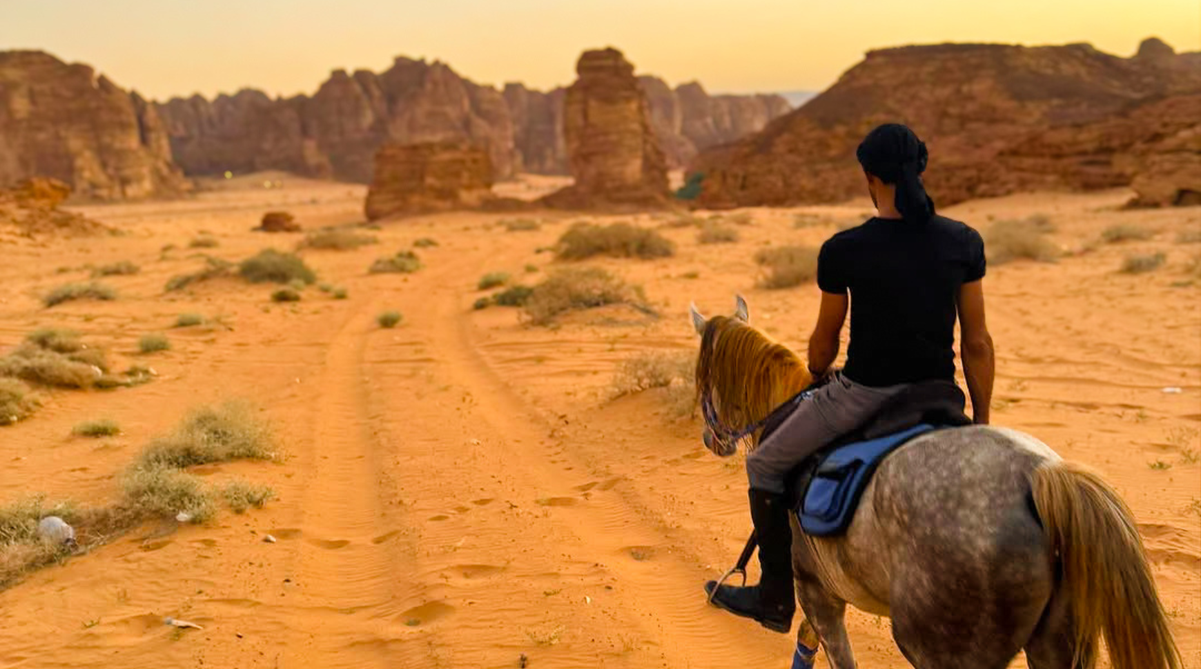 A person riding a horse across a vast desert landscape under a clear blue sky.