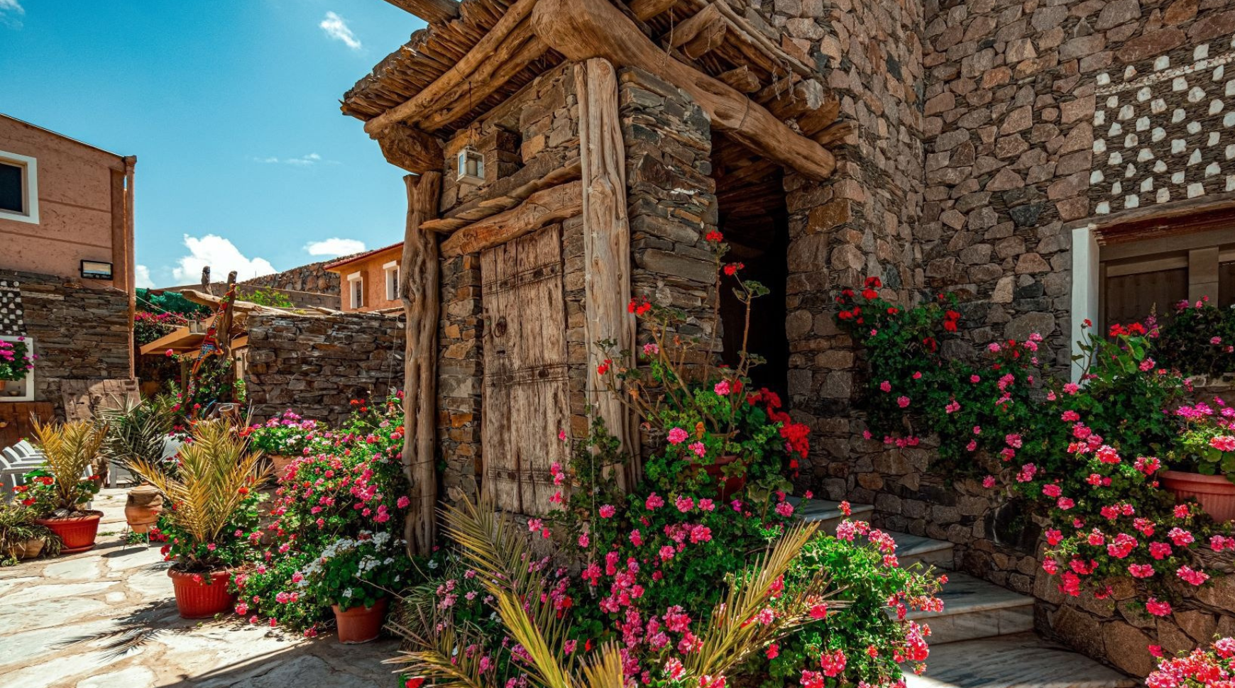 A stone house surrounded by colorful flowers and lush plants in the foreground.