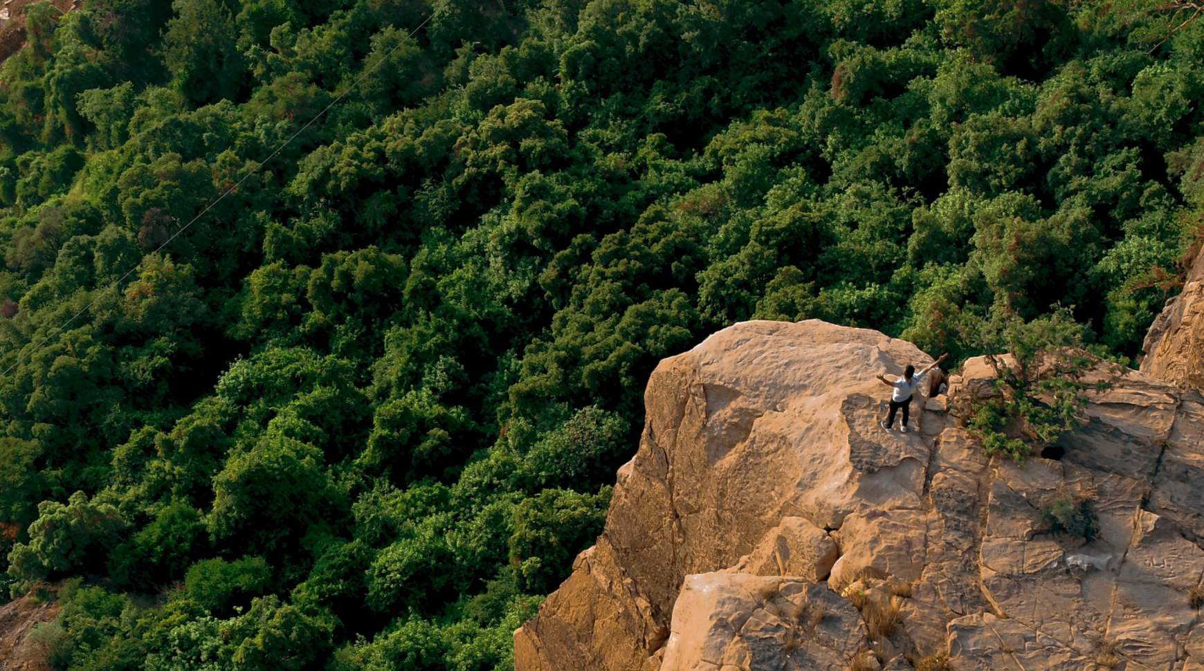 A man stands confidently atop a large rock, overlooking the surrounding landscape.
