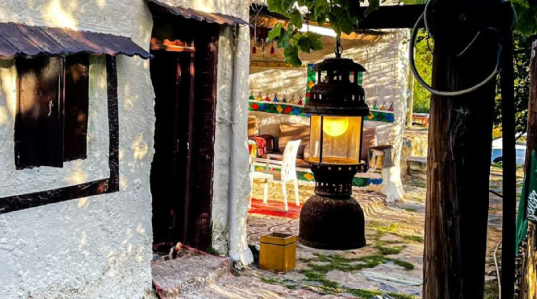 A small house with a lantern hanging from the roof, casting a warm glow in the evening light.