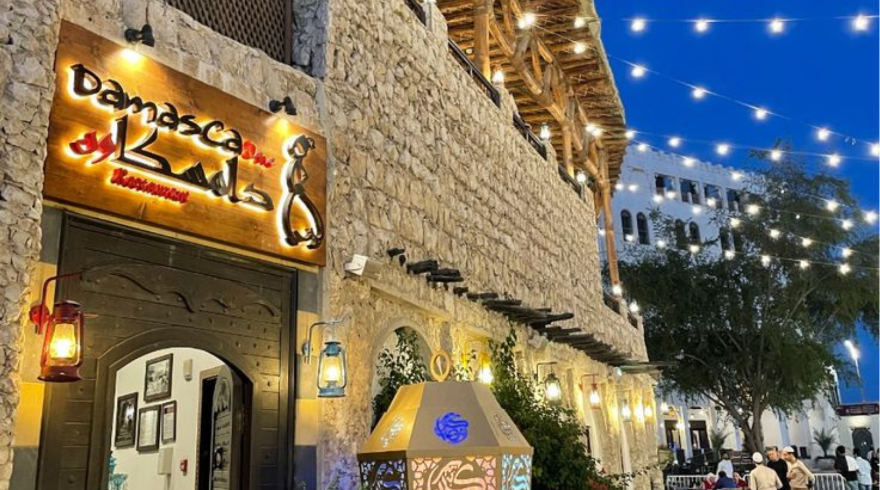 The entrance of a restaurant adorned with string lights illuminating the street, creating a welcoming atmosphere.
