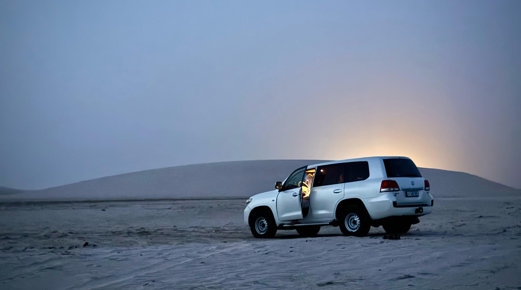 A white SUV parked on the sand, silhouetted against a vibrant sunset sky.