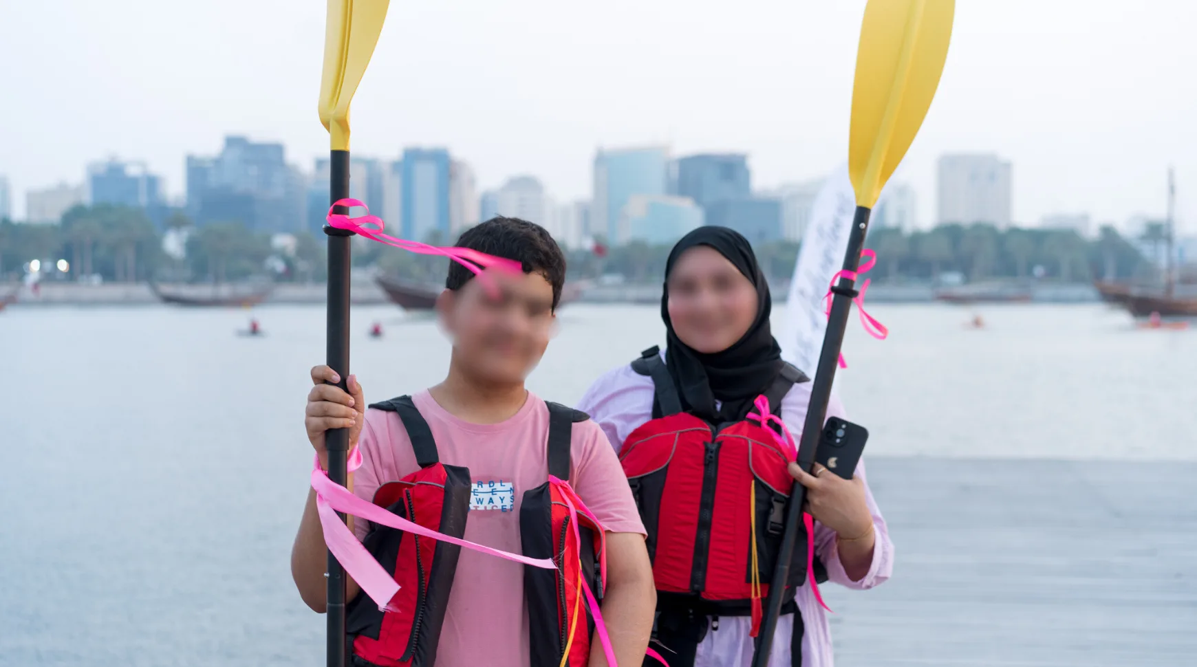 Two individuals stand on a dock, each holding a paddle, preparing for a water activity.