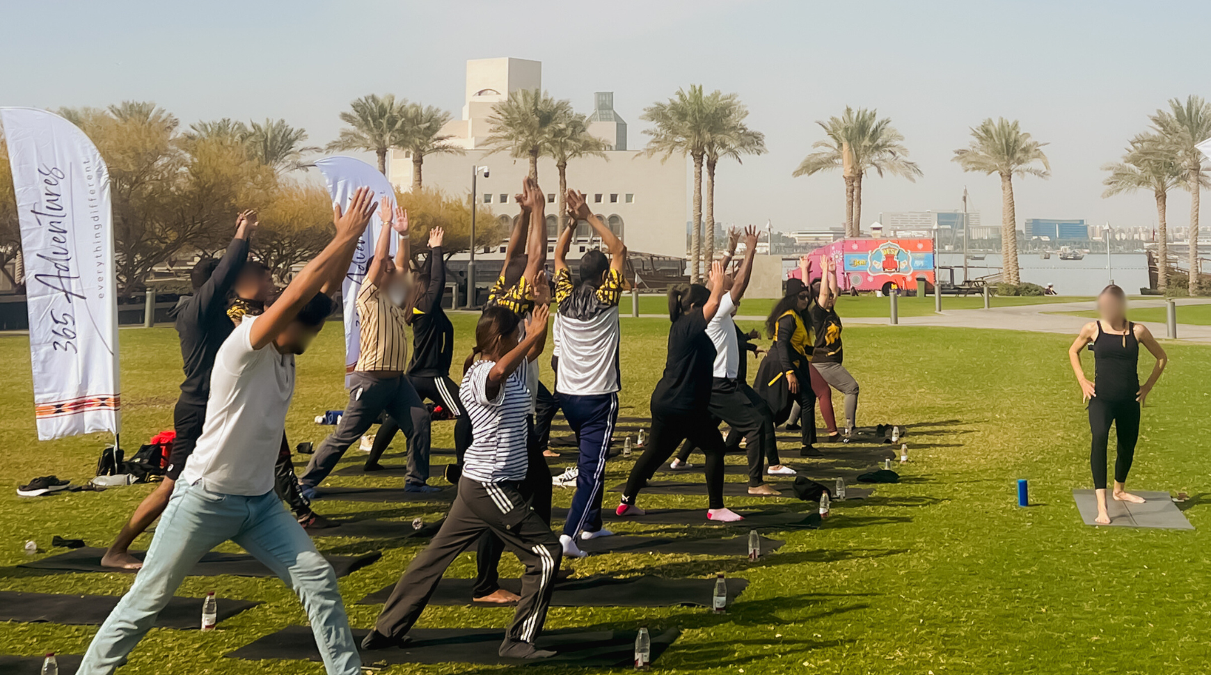 A group of people practicing yoga in a park surrounded by tall palm trees under a clear blue sky.