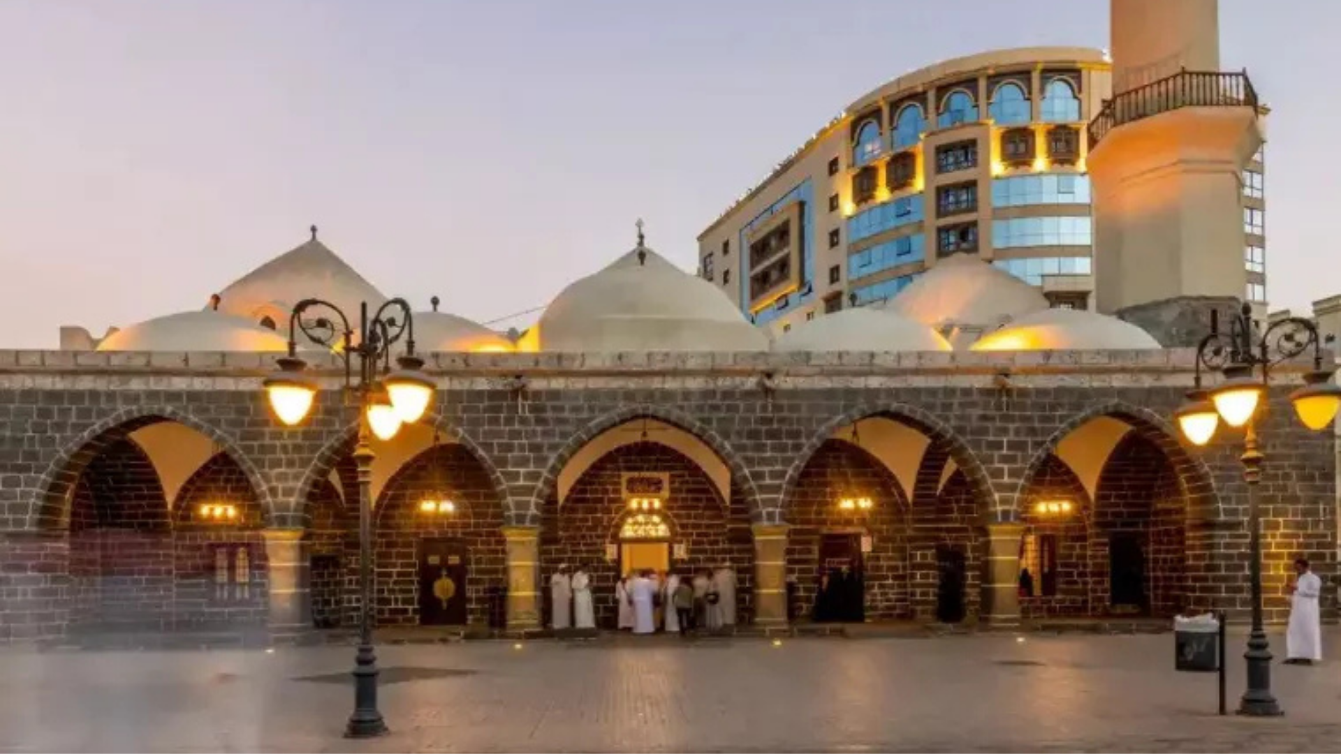 A large mosque featuring multiple domes and illuminated with numerous lights, showcasing intricate architectural design.