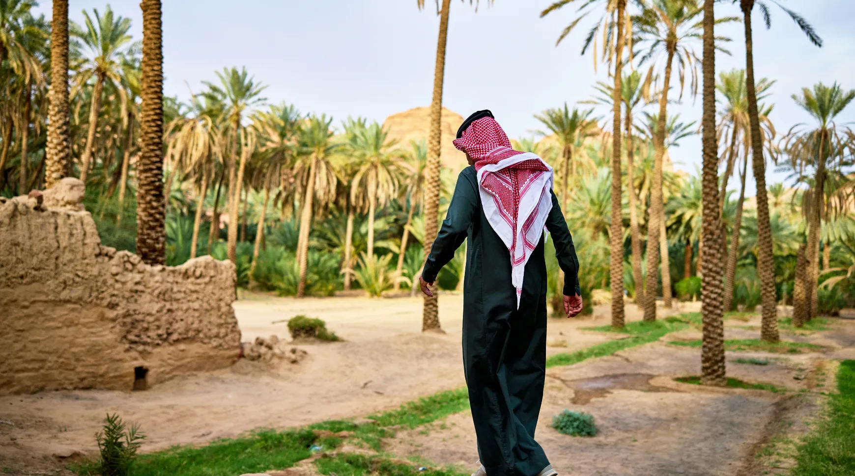 A man in traditional attire walks through a vast desert landscape under a clear blue sky.