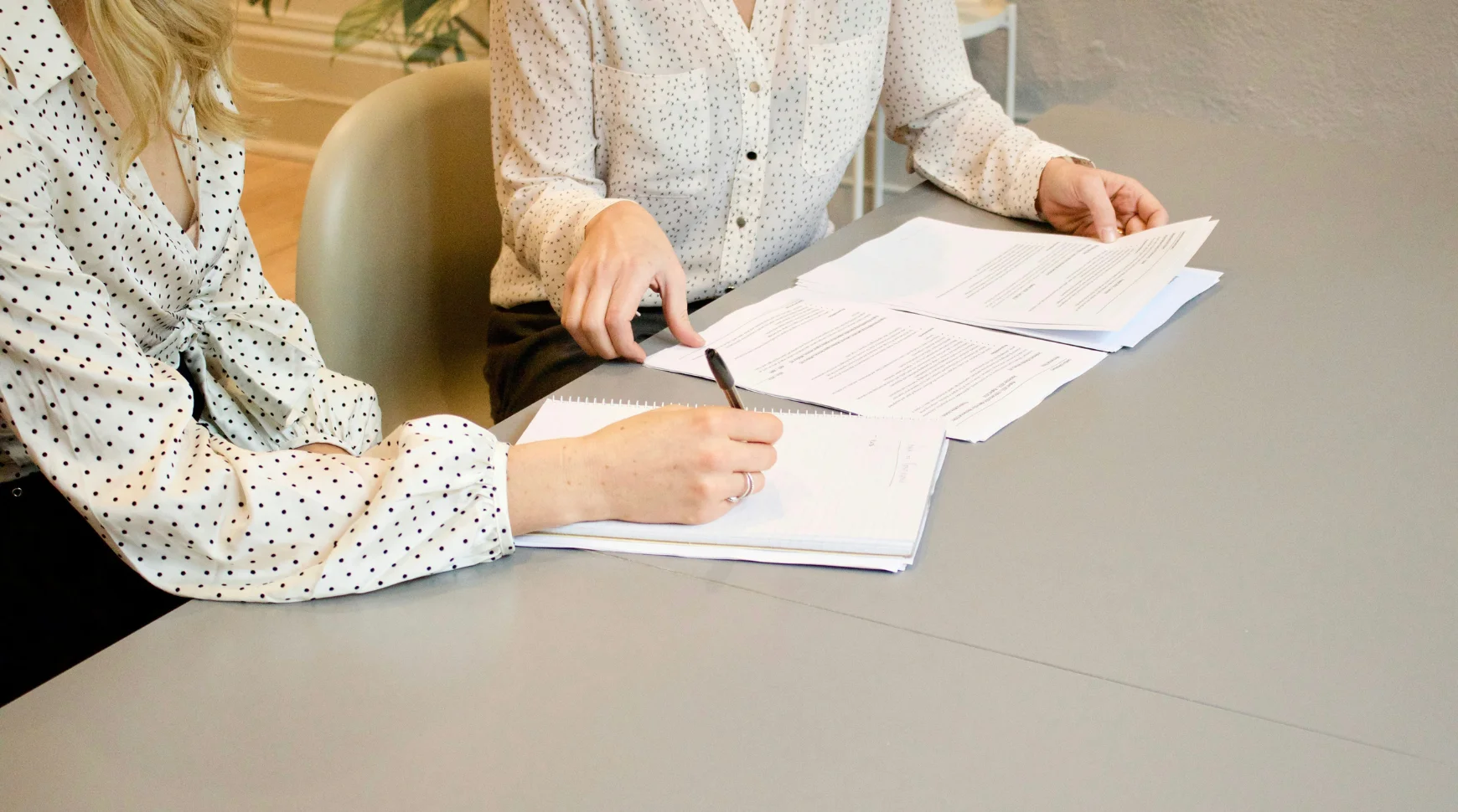 Two women seated at a table, reviewing documents and discussing their contents.